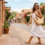 Woman in white linen midi dress walking down a sunlit street on a hot summer day