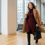 Professional woman in a burgundy wrap dress layered with a turtleneck, tights, boots, and camel coat for the office in winter.
