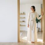 Tall woman in a flowing cream maxi dress standing in a sunlit doorway